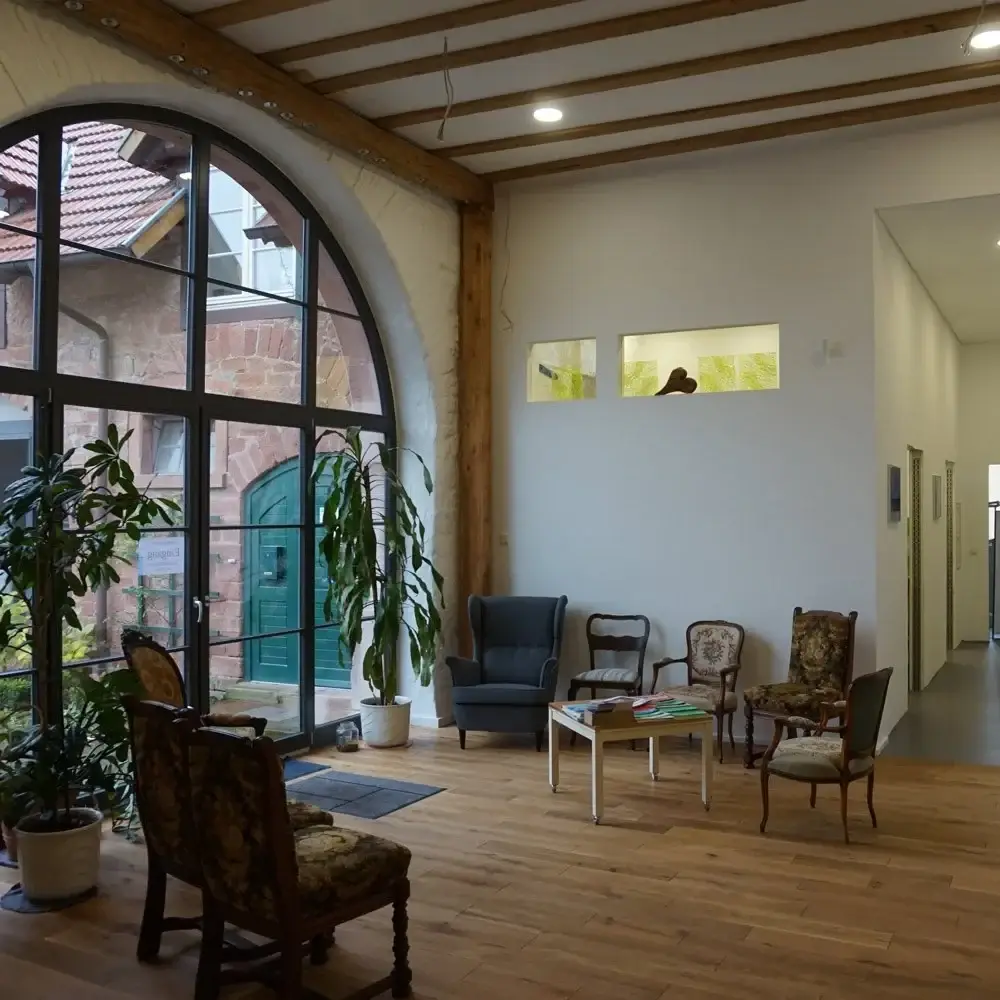 Wartebereich mit großem Rundbogenfenster und Holzbalkendecke